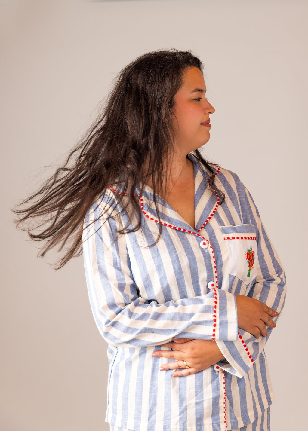 Woman wearing a blue and white striped pajama top with a red flower design on a plain background