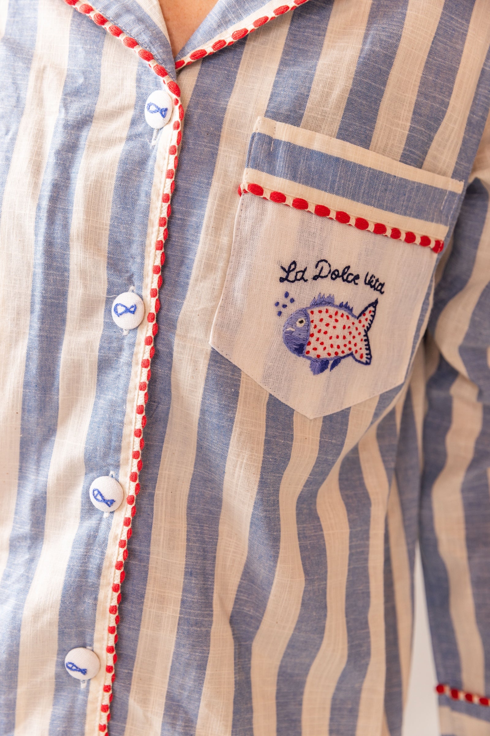 Close-up of a striped LONG shirt with a pocket featuring an embroidered design and text. LA DOLCE VITA