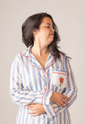 Woman wearing a blue and white striped pajama set with red trim on a plain background