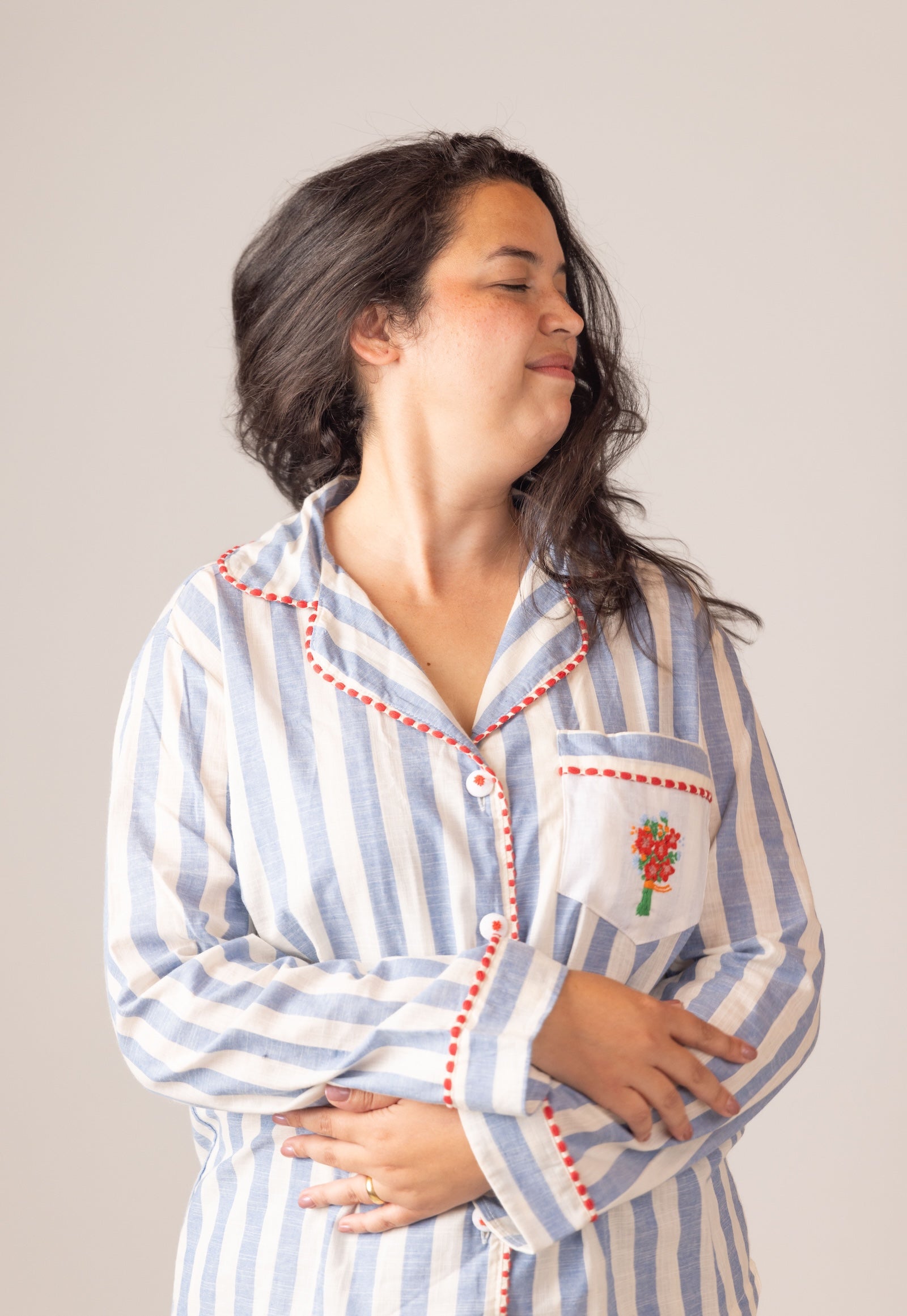 Woman wearing a blue and white striped pajama set with red trim on a plain background