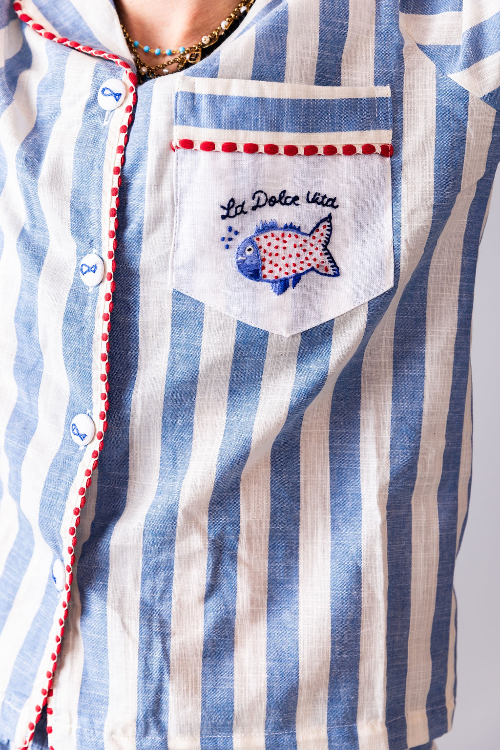 Close-up of a blue and white striped shirt with a EMBROIDERED fish design and text on the chest pocket.
