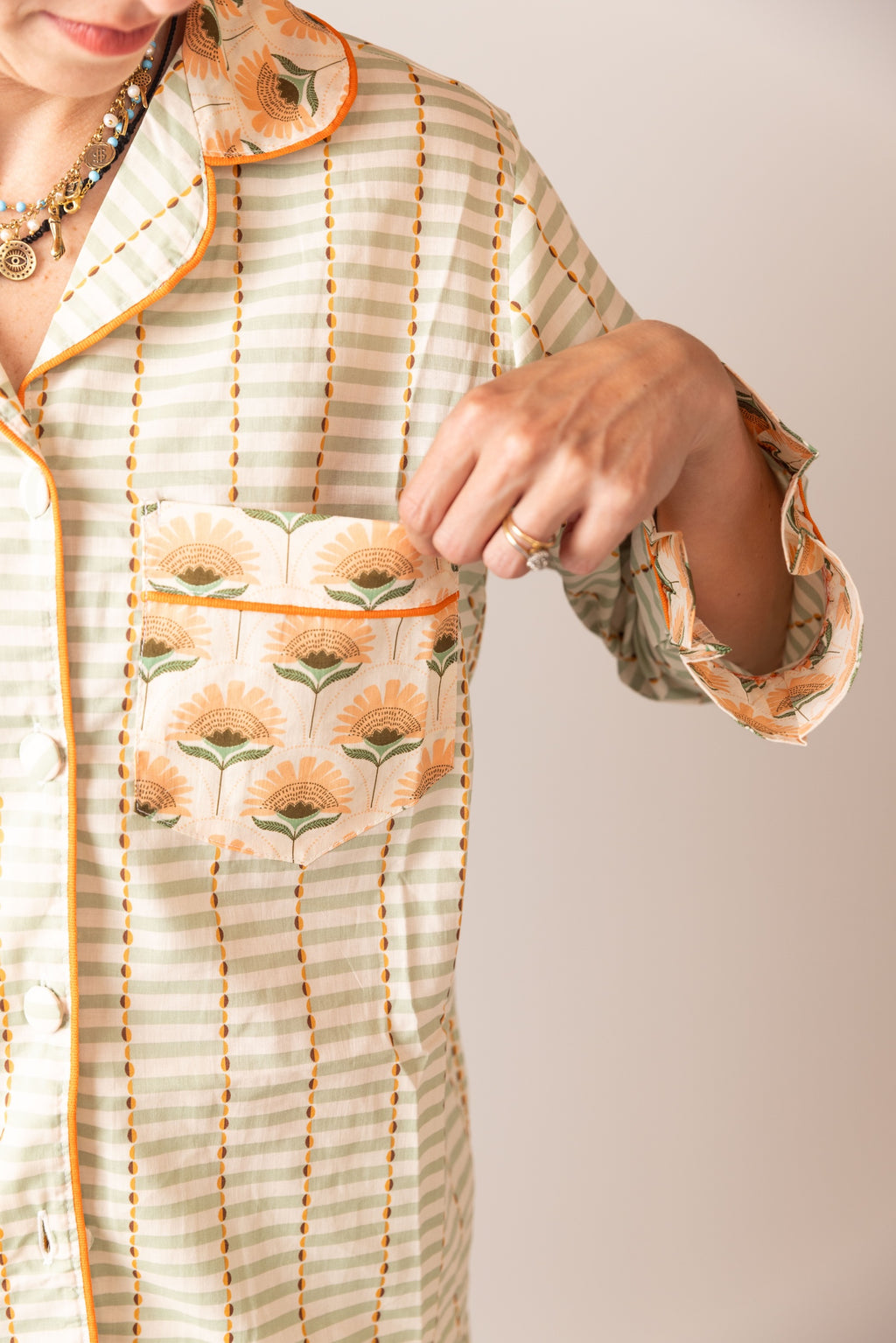 Person wearing a light-colored outfit with floral patterns on a plain background. POCKET DETAIL 