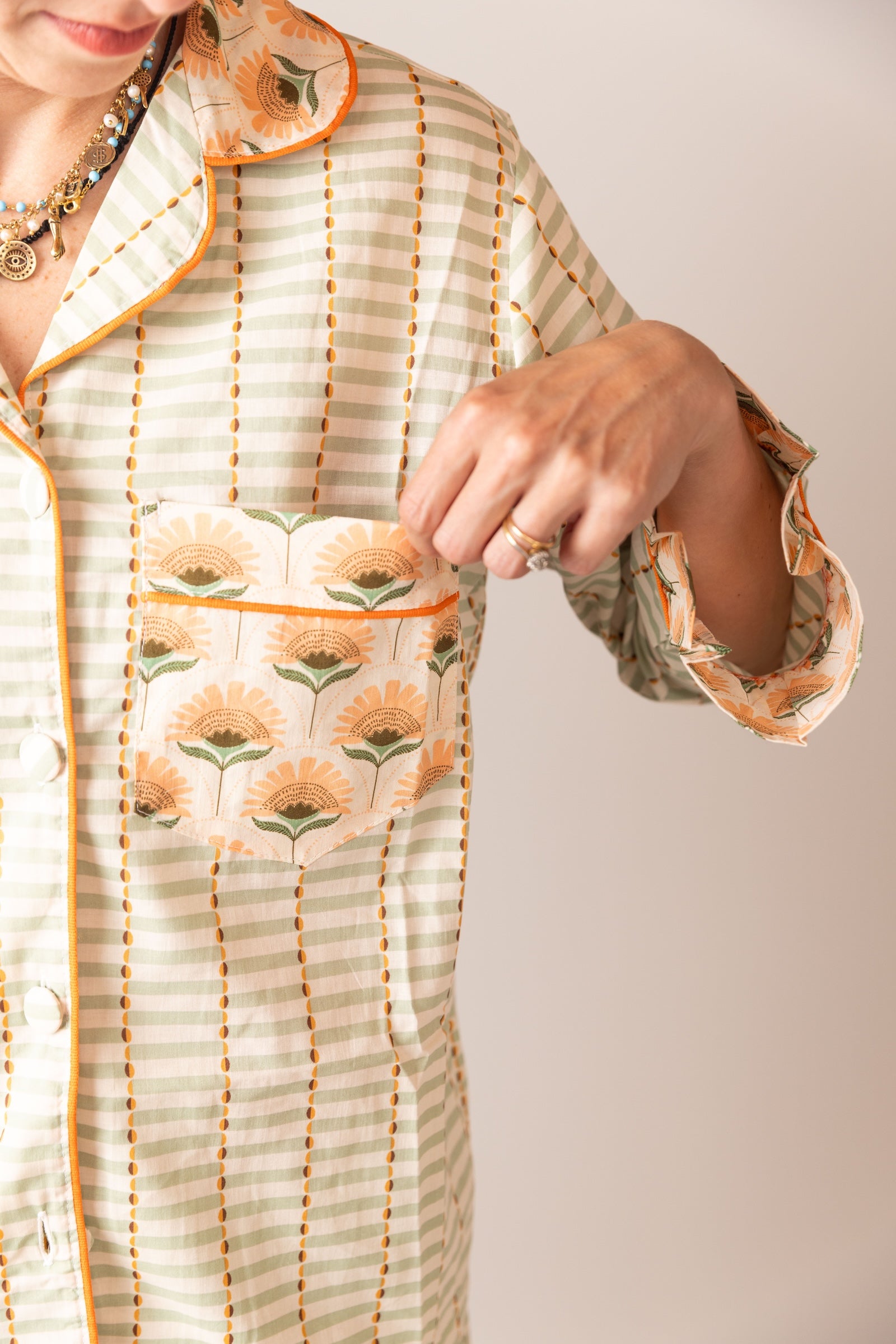 Person wearing a light-colored outfit with floral patterns on a plain background. POCKET DETAIL 