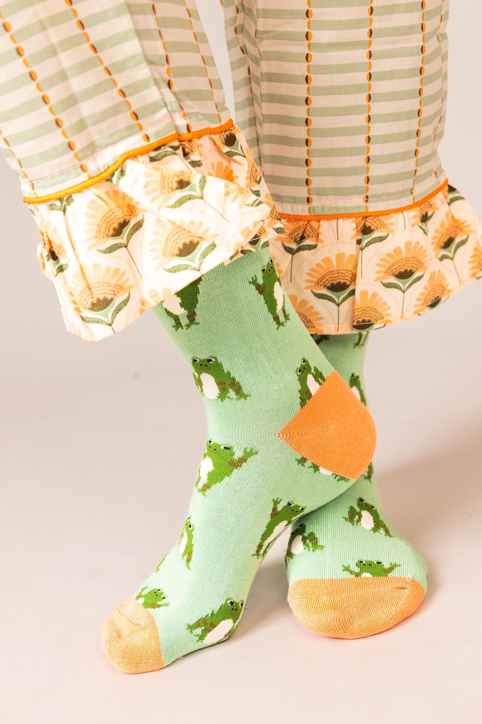 Person wearing green socks with orange accents and floral-fan-patterned pants on a neutral background