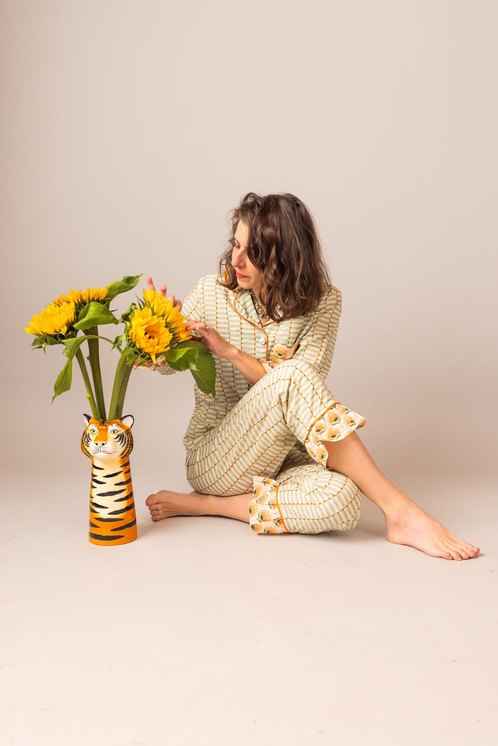 Woman in a FAN patterned outfit holding sunflowers next to a tiger-shaped vase on a plain background