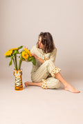 Woman in a FAN patterned outfit holding sunflowers next to a tiger-shaped vase on a plain background