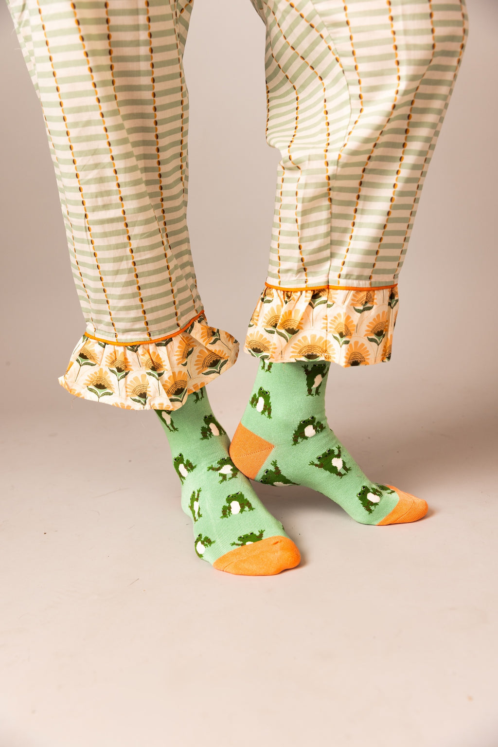 Green socks with orange toes and heels worn with plaid pants on a neutral background