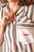Person wearing a striped garment with a pocket featuring a COSMOPOLITAN glass design.