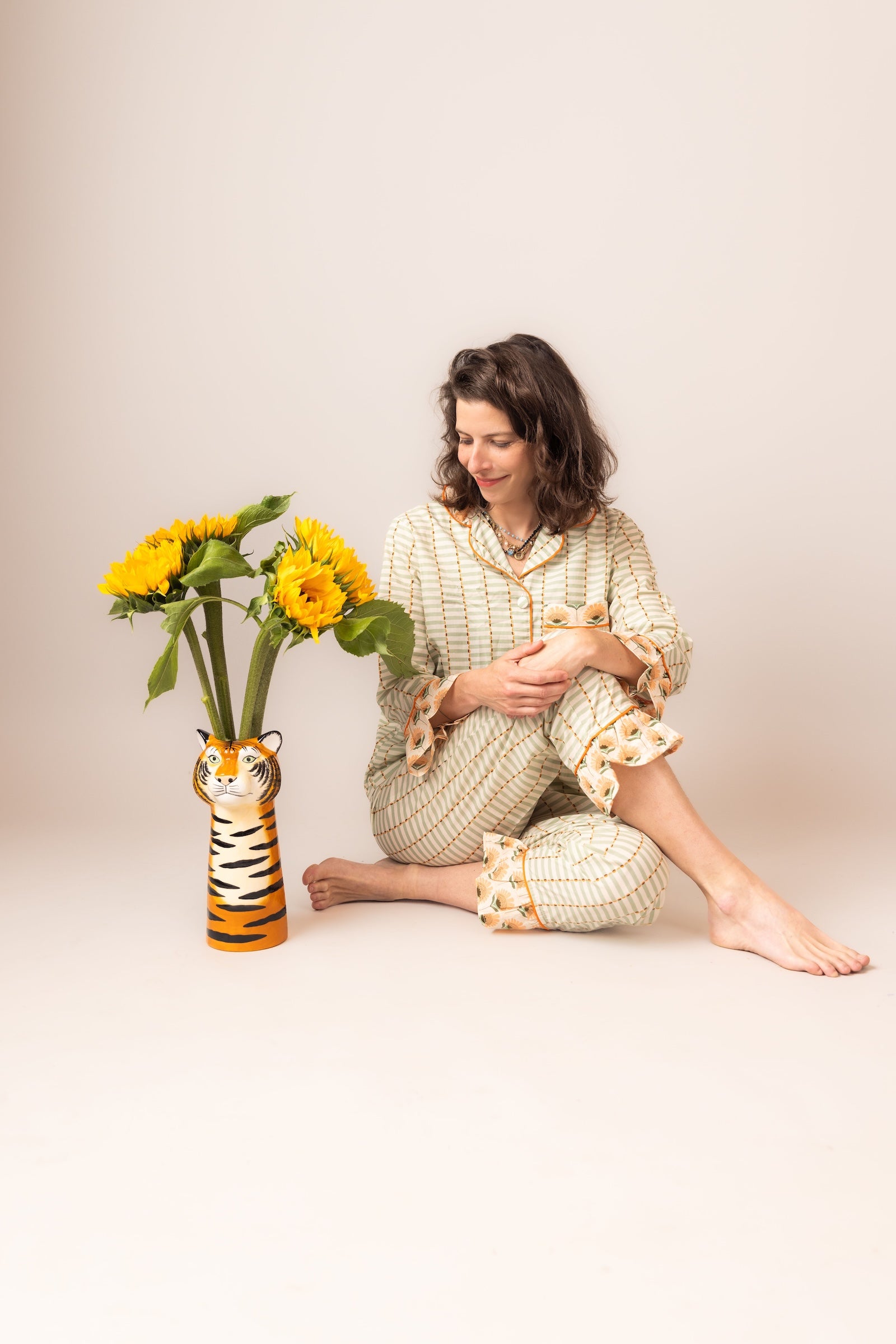 Woman in a cozy outfit sitting with sunflowers and a tiger vase on a plain background