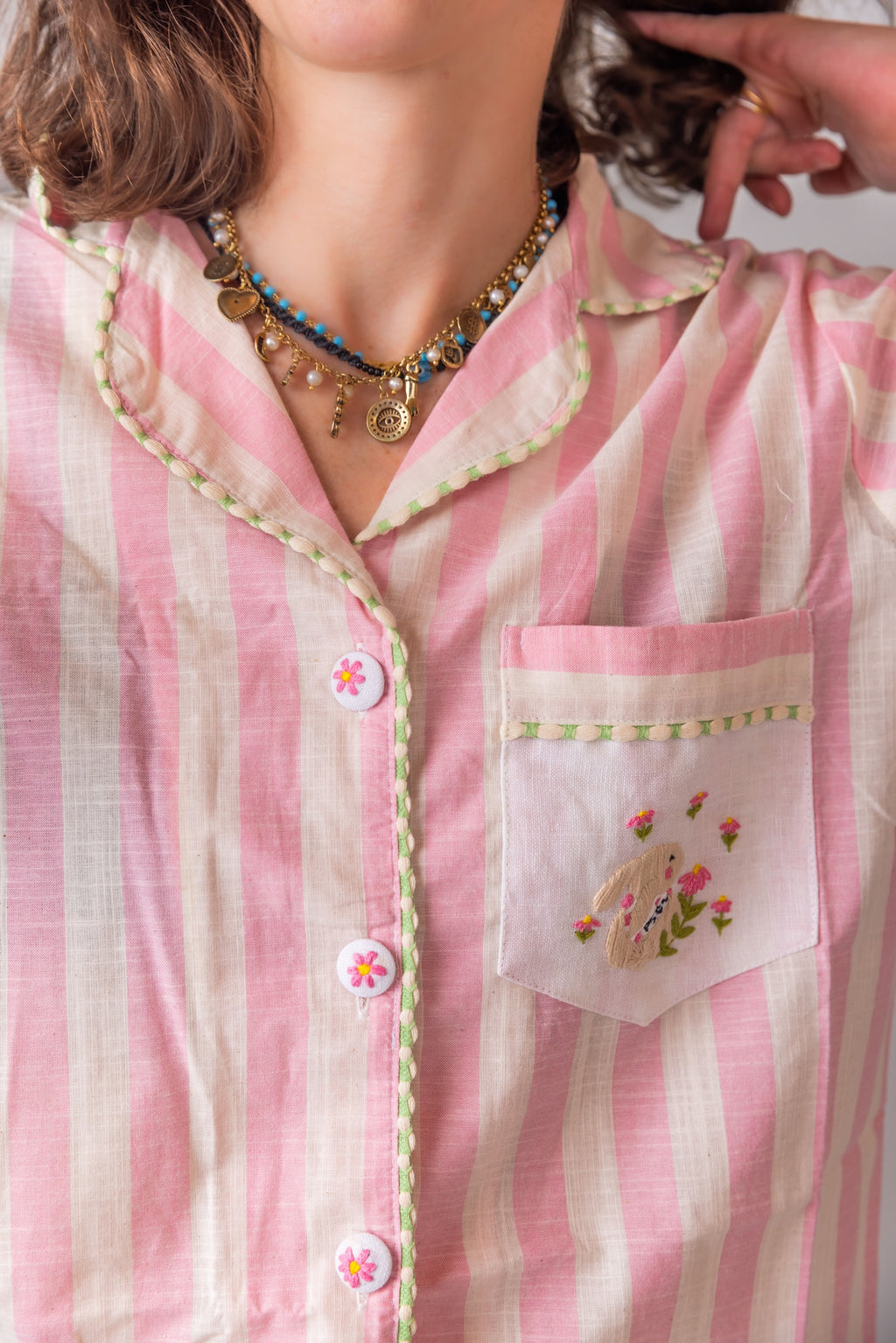 Close-up of a person wearing a pink and white striped shirt with floral embroidery on the pocket.